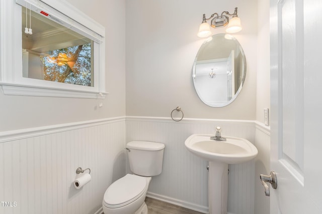 half bath with toilet and a wainscoted wall