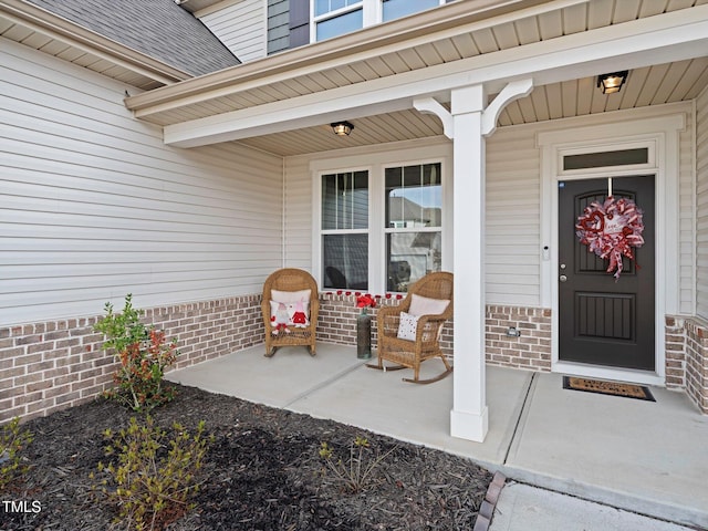 entrance to property with a porch, roof with shingles, and brick siding