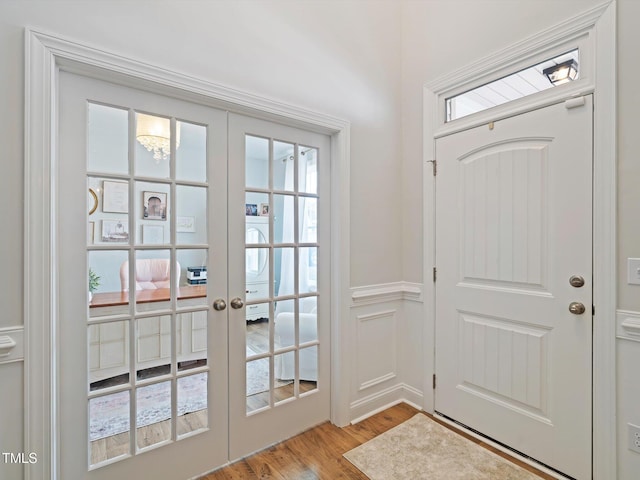 doorway to outside with light wood-style floors, french doors, wainscoting, and a decorative wall