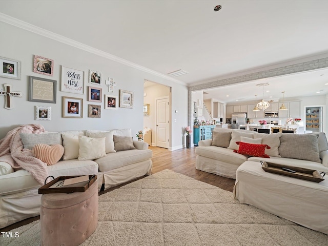 living area with light wood finished floors, visible vents, an inviting chandelier, stairs, and crown molding