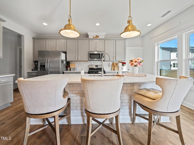 kitchen featuring a center island with sink, visible vents, decorative backsplash, appliances with stainless steel finishes, and gray cabinetry