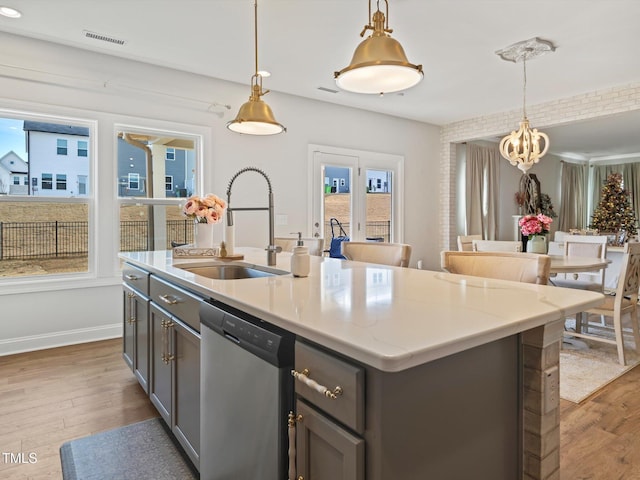 kitchen featuring wood finished floors, stainless steel dishwasher, a sink, and gray cabinetry