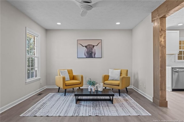 living area featuring light wood-type flooring, a textured ceiling, and baseboards