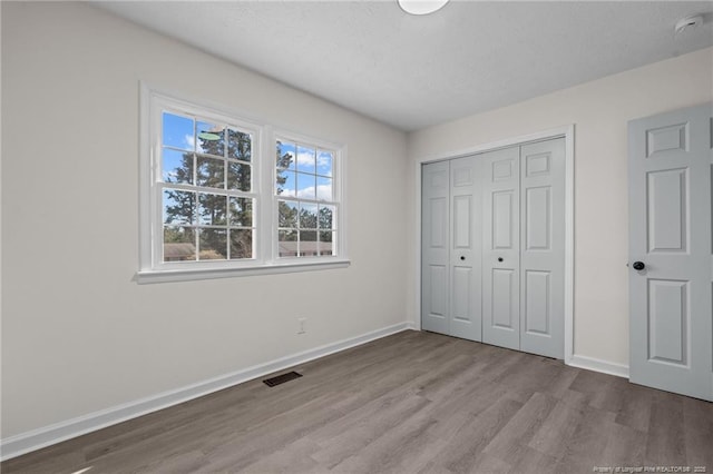 unfurnished bedroom featuring a closet, visible vents, light wood-style flooring, and baseboards