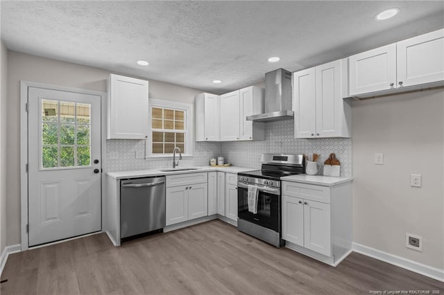 6815 Radial Dr, Fayetteville, NC 28311 - kitchen featuring appliances with stainless steel finishes, wall chimney exhaust hood, wood finished floors, light countertops, and white cabinetry