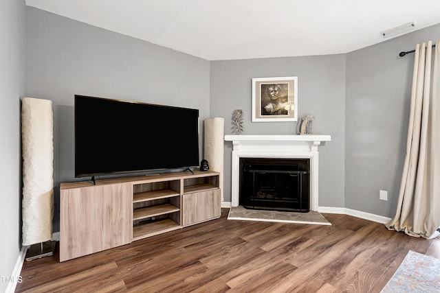 unfurnished living room with visible vents, a fireplace with raised hearth, baseboards, and dark wood-style flooring