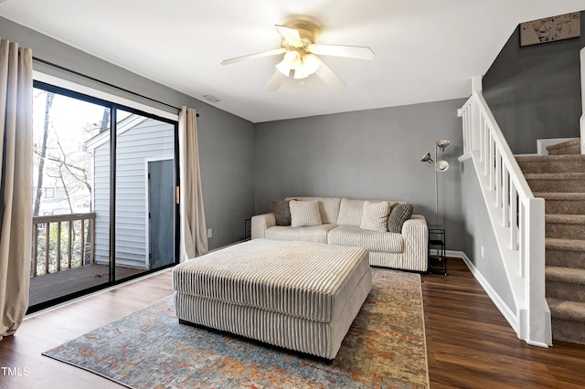 living area with stairway, wood finished floors, a wealth of natural light, and ceiling fan