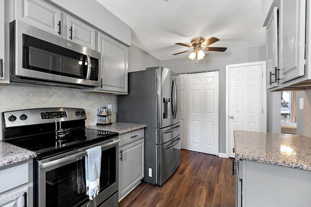 kitchen featuring dark wood-style floors, a ceiling fan, light stone countertops, stainless steel appliances, and decorative backsplash