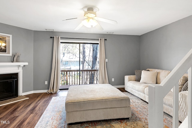 living area with visible vents, a fireplace with raised hearth, a ceiling fan, dark wood finished floors, and baseboards