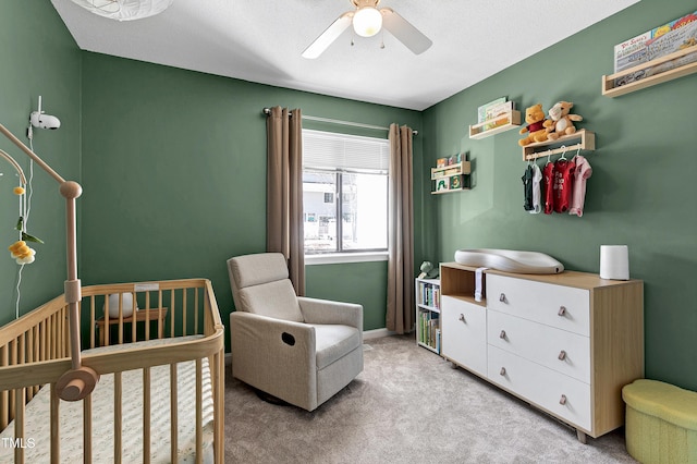 bedroom featuring light colored carpet, a ceiling fan, and a nursery area