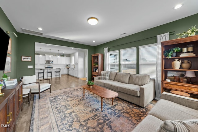 living area with recessed lighting, visible vents, and wood finished floors