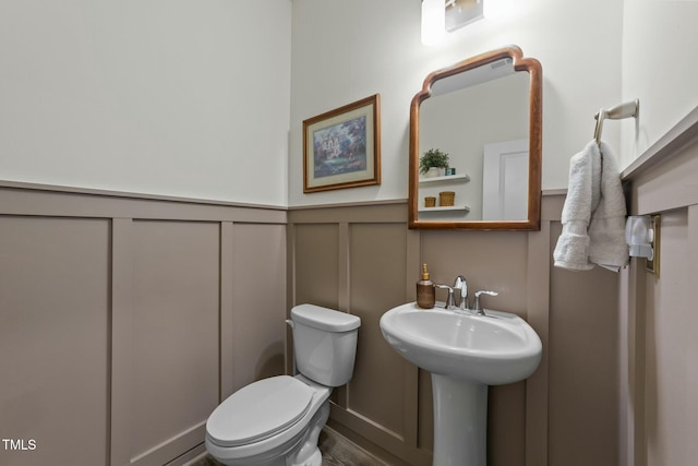 bathroom with wainscoting, a decorative wall, and toilet