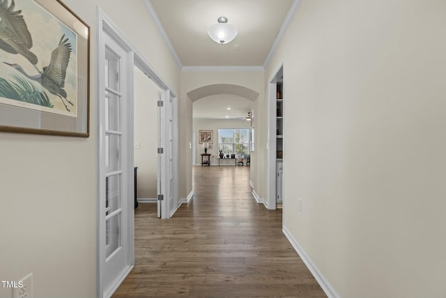 corridor with dark wood-style floors, arched walkways, ornamental molding, and baseboards