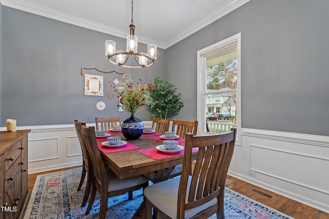 dining space featuring wood finished floors, a wainscoted wall, visible vents, crown molding, and a notable chandelier