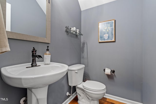 half bath featuring wood finished floors, toilet, baseboards, and a sink