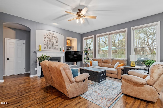 living room featuring hardwood / wood-style flooring, arched walkways, a fireplace, baseboards, and ceiling fan