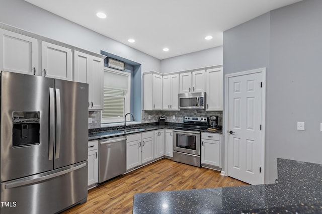 kitchen featuring decorative backsplash, wood finished floors, white cabinets, stainless steel appliances, and a sink