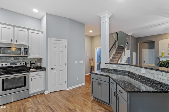 kitchen with dark stone countertops, appliances with stainless steel finishes, white cabinets, light wood finished floors, and decorative backsplash