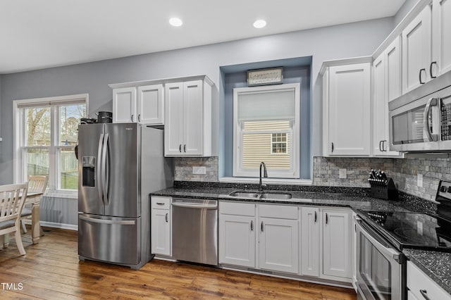 kitchen featuring dark stone countertops, dark wood-style floors, appliances with stainless steel finishes, and a sink