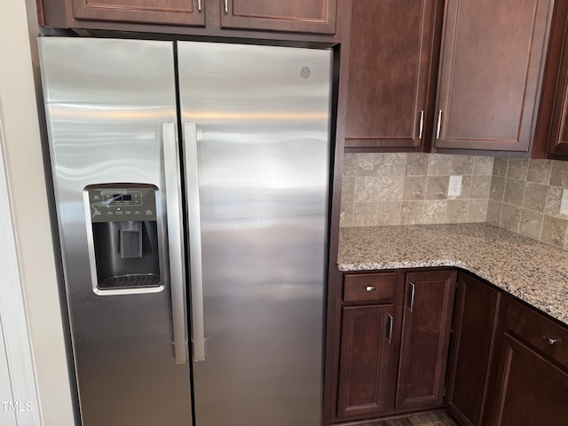 kitchen featuring light stone counters, backsplash, stainless steel refrigerator with ice dispenser, and dark brown cabinets