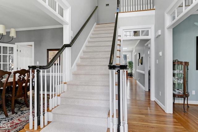 stairs featuring baseboards, crown molding, a towering ceiling, and wood finished floors