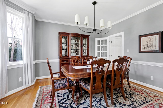 dining room featuring light wood-style flooring, a notable chandelier, baseboards, and ornamental molding