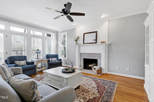 living room with a fireplace, light wood-style floors, ceiling fan, and crown molding