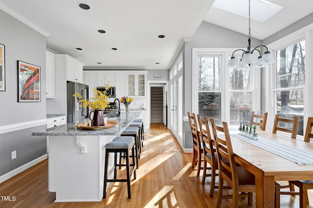 dining room featuring lofted ceiling with skylight, baseboards, light wood-type flooring, and an inviting chandelier