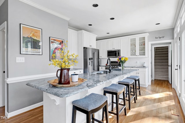 kitchen featuring light wood-style flooring, ornamental molding, a sink, appliances with stainless steel finishes, and a breakfast bar area