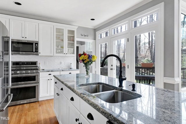 kitchen featuring a sink, backsplash, appliances with stainless steel finishes, white cabinets, and glass insert cabinets