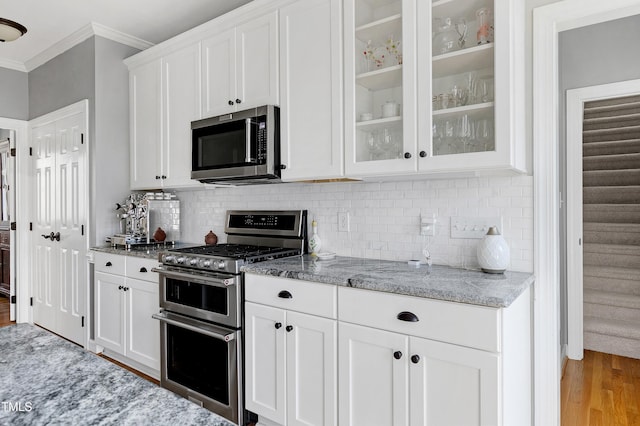 kitchen with light wood-style flooring, ornamental molding, light stone counters, stainless steel appliances, and white cabinets