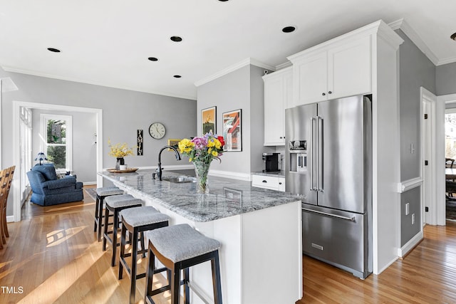 kitchen with light wood-style flooring, light stone countertops, high quality fridge, and a sink