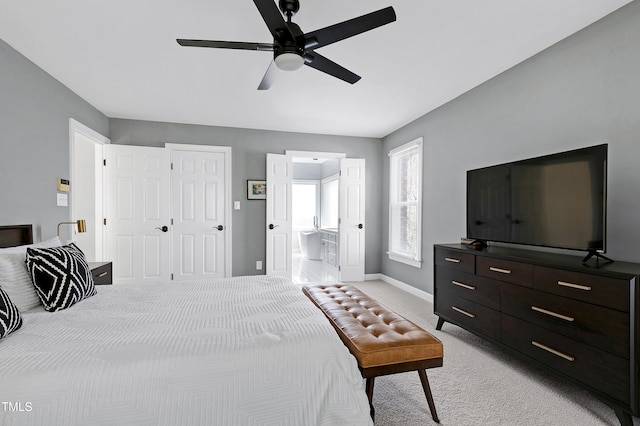 bedroom with baseboards, light carpet, a ceiling fan, and ensuite bathroom