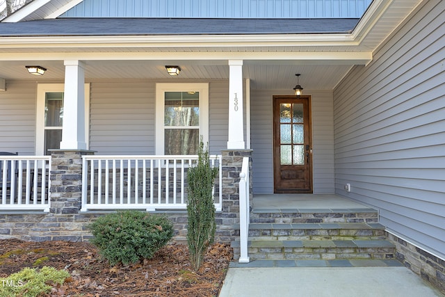 entrance to property with a porch, stone siding, and roof with shingles