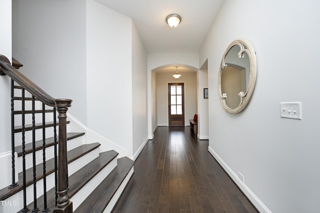 hallway with arched walkways, stairs, baseboards, and hardwood / wood-style floors