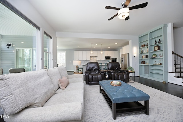 living area with recessed lighting, light wood-style floors, baseboards, ceiling fan, and stairs