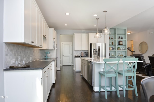 kitchen featuring dark wood-style flooring, white cabinets, appliances with stainless steel finishes, pendant lighting, and a kitchen bar