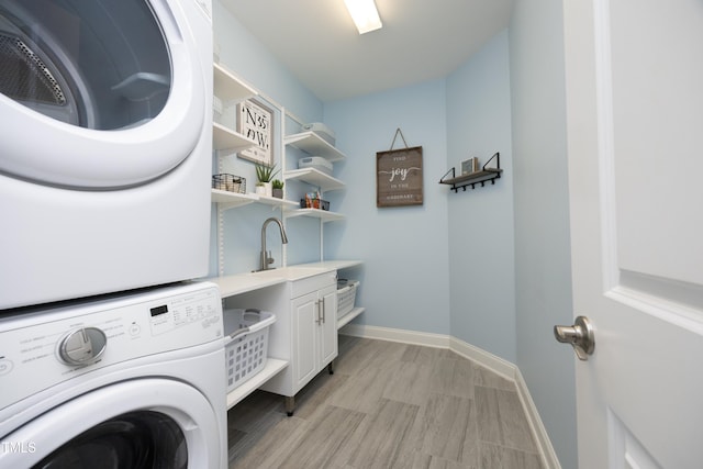 washroom featuring light wood finished floors, baseboards, stacked washer and dryer, cabinet space, and a sink