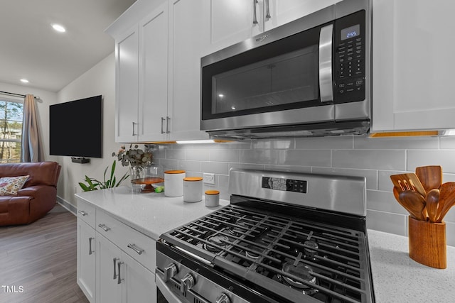 kitchen featuring stainless steel appliances, backsplash, open floor plan, white cabinets, and wood finished floors