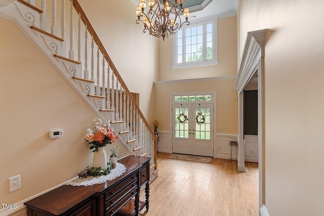 entryway with a wainscoted wall, light wood-style flooring, ornamental molding, an inviting chandelier, and stairs