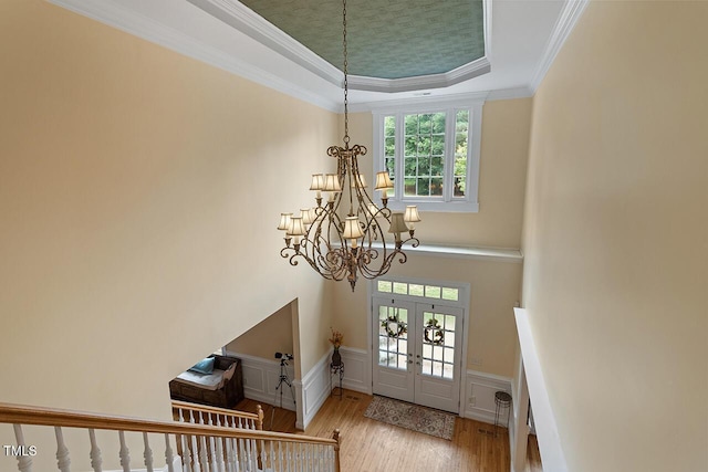 entryway featuring a tray ceiling, a wainscoted wall, crown molding, a notable chandelier, and wood finished floors