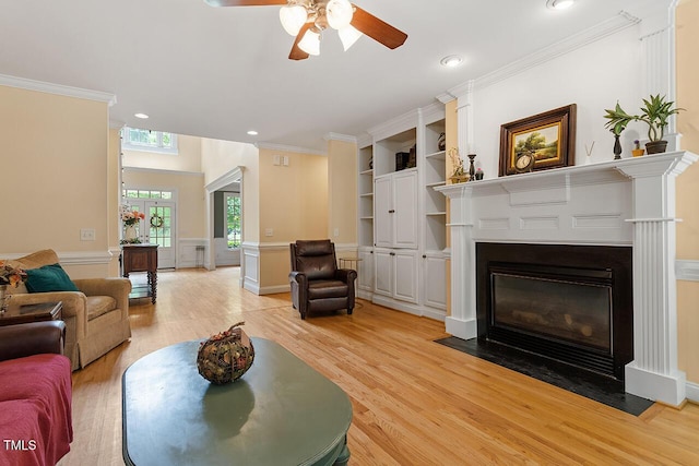 living area featuring light wood finished floors, wainscoting, a fireplace with flush hearth, and crown molding