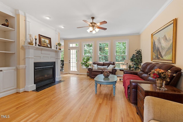 living room featuring built in shelves, ornamental molding, a fireplace with flush hearth, ceiling fan, and light wood-type flooring