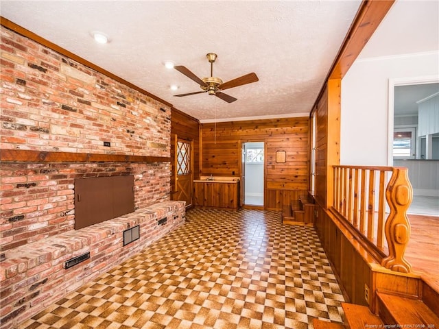 unfurnished living room with ceiling fan, wooden walls, ornamental molding, and a textured ceiling