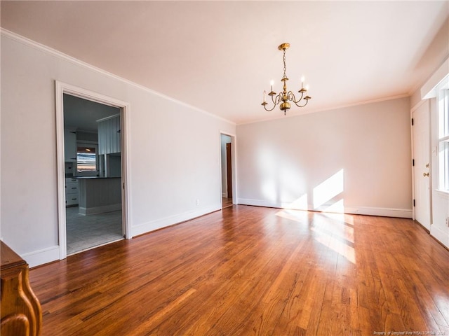 empty room featuring crown molding, wood finished floors, and a notable chandelier