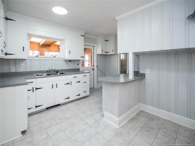 kitchen featuring crown molding, dark countertops, white cabinetry, and a sink