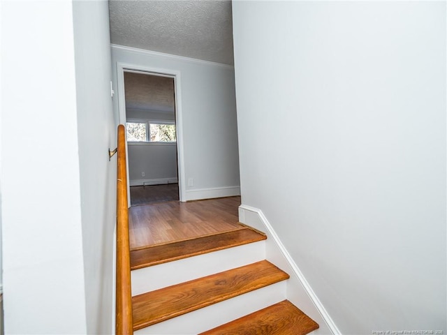 stairway featuring a textured ceiling, wood finished floors, and baseboards