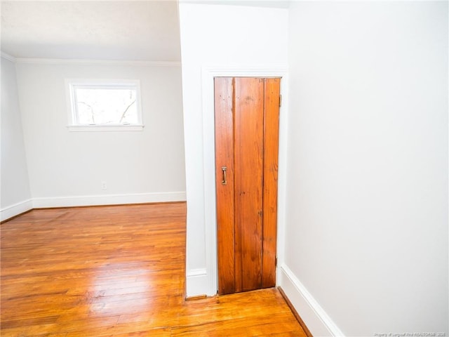 empty room featuring light wood-type flooring, baseboards, and crown molding