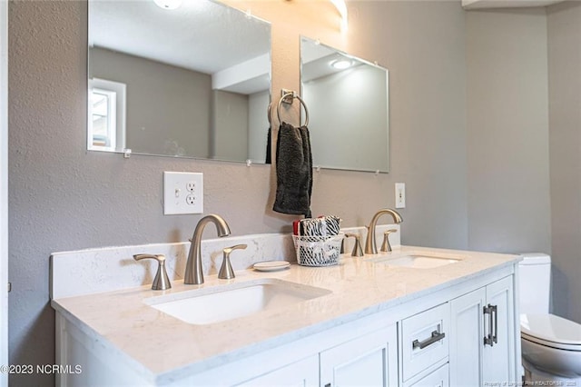 full bathroom featuring toilet, double vanity, a sink, and a textured wall