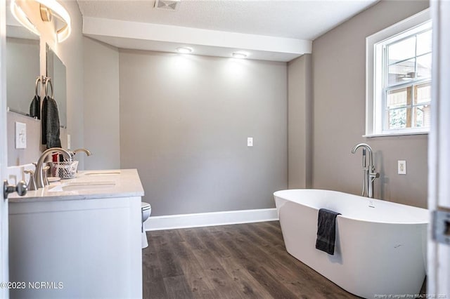 full bathroom featuring double vanity, a soaking tub, toilet, a sink, and wood finished floors